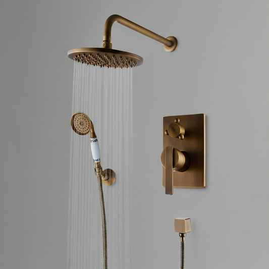 The Rozin Antique Brass Shower System With Handheld Shower includes a round rain shower head, flexible hose hand shower, and wall-mounted control knobs, all showcased against a plain gray wall.