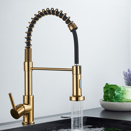 The Quyanre Pro Spring Neck Pull-Down Kitchen Faucet features a gold finish, flexible black coiled hose, and pull-down spray head. Water streams into the sink as vegetables and a white bowl sit in the background, adding modern convenience.