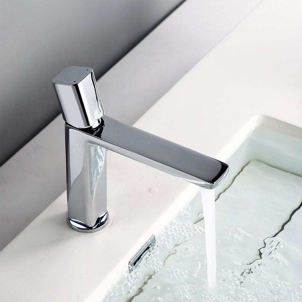 A sleek, modern Polished Chrome Bathroom Sink Faucet from Morsale.com, featuring a cylindrical base and a straight spout, pours a stream of water into a white sink. The background is a plain light gray wall.