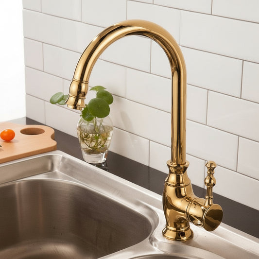 The Tiqui Maison Polished Gold Kitchen Faucet with a curved spout and pull-down spray head is installed on a stainless steel sink. White subway tiles and a small plant in a glass vase complete the modern look.