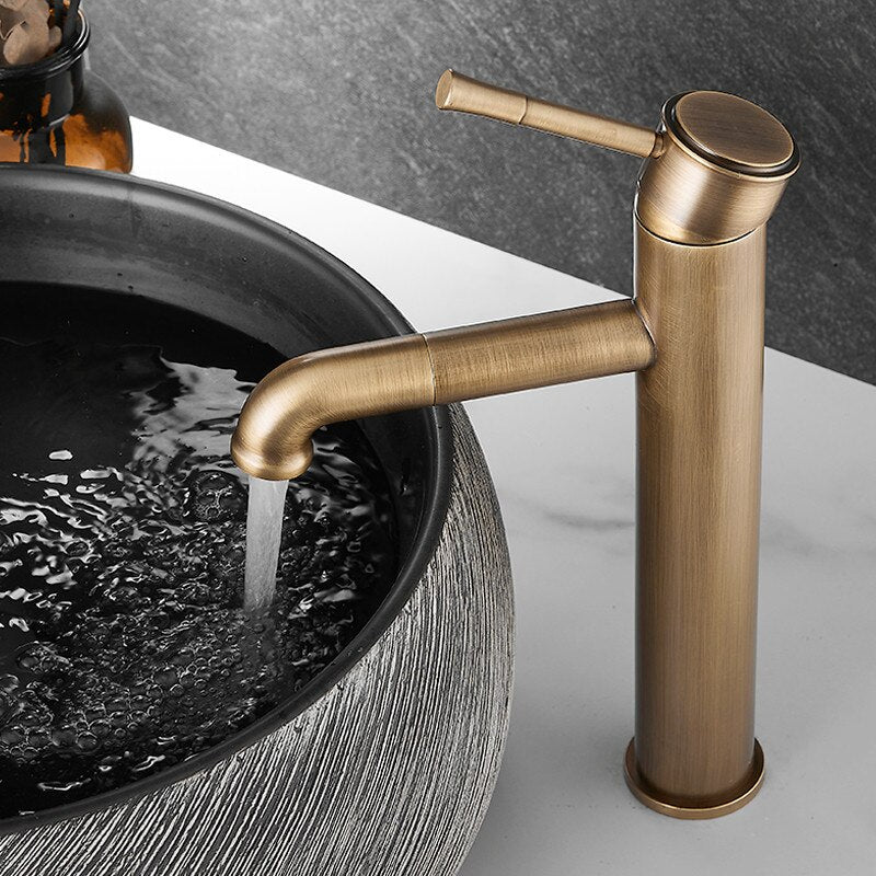 The Tiqui Antique Bronze Single‑Handle Bathroom Faucet stands tall, running water into a round, textured basin sink set on a white countertop against a dark background.