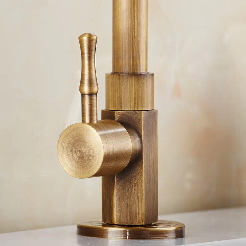 Close-up of the ZGRK Antique Brass Single-Handle Kitchen Faucet, featuring a brushed finish and vertical lever, mounted on a light countertop. The vintage-style design highlights both cylindrical and square details.