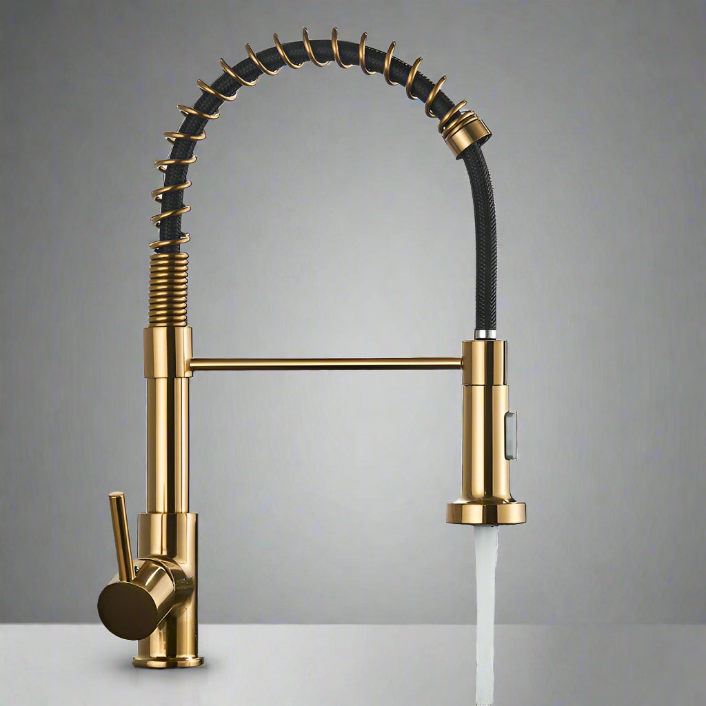 The Quyanre Pro Spring Neck Pull-Down Kitchen Faucet, in a modern gold finish with a flexible coiled neck and single lever handle, is mounted on a white countertop. Water streams from its pull-down spray head against a plain gray wall.