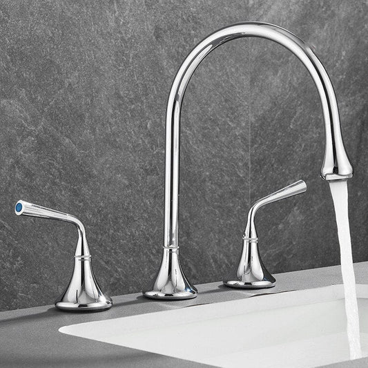 The Mike Jake Maison Widespread Bathroom Faucet, a modern silver double-handle design with a high-arc spout, runs water into a white sink set against a gray stone background.