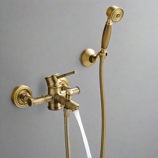 The Ellen Antique Brass Shower & Tub Faucet System features a wall-mounted design with water flowing from the main spout and a handheld shower that rests conveniently in its holder beside the faucet.