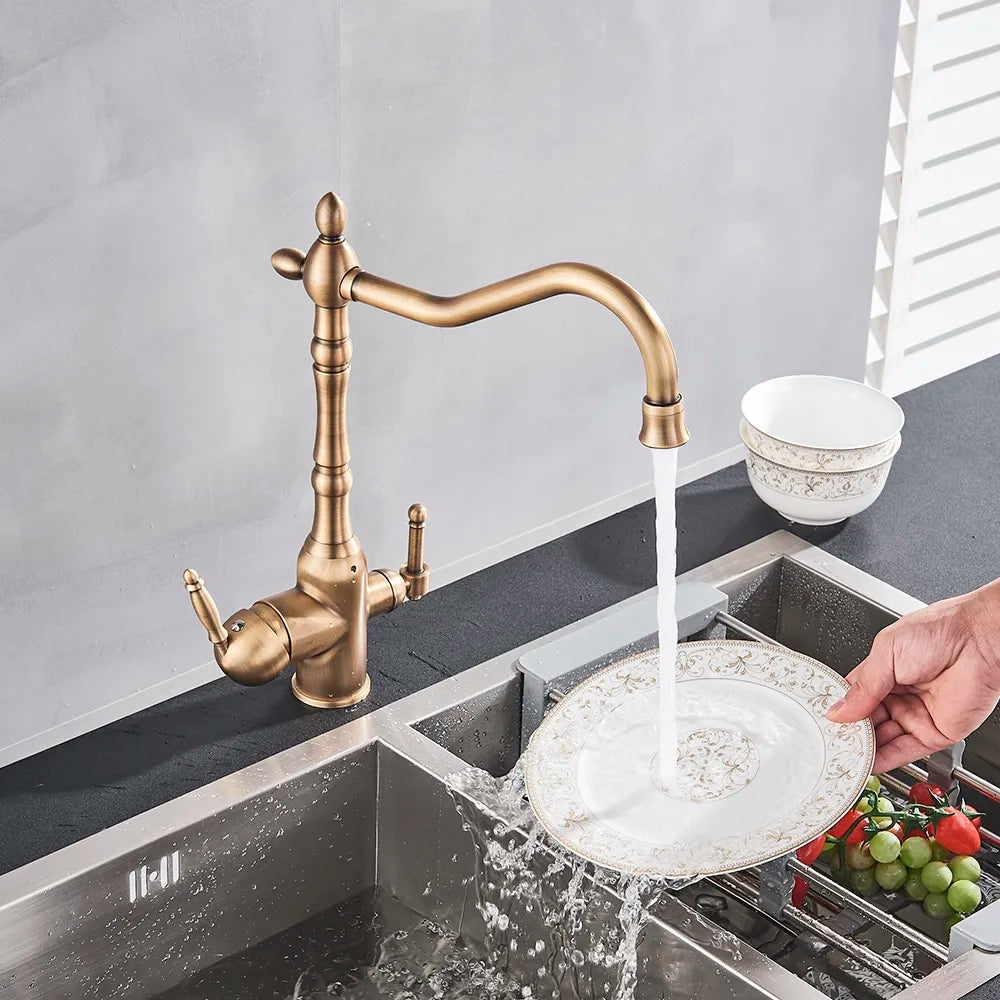 The Uythner Antique Bronze Kitchen Faucet with Filtered Water Tap features a sleek vintage design with an L-shaped spout. It includes two handles: a lever handle and a smaller knob beside it, set against a plain light gray wall.