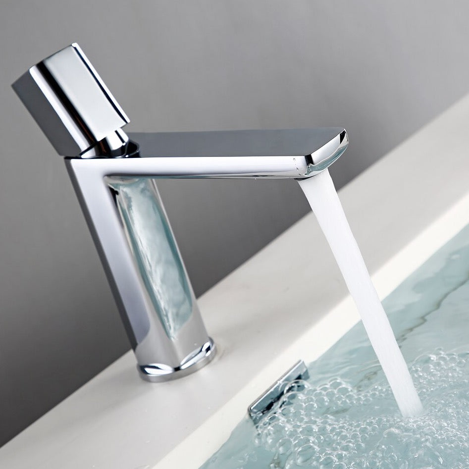 A sleek, modern Polished Chrome Bathroom Sink Faucet from Morsale.com, featuring a cylindrical base and a straight spout, pours a stream of water into a white sink. The background is a plain light gray wall.
