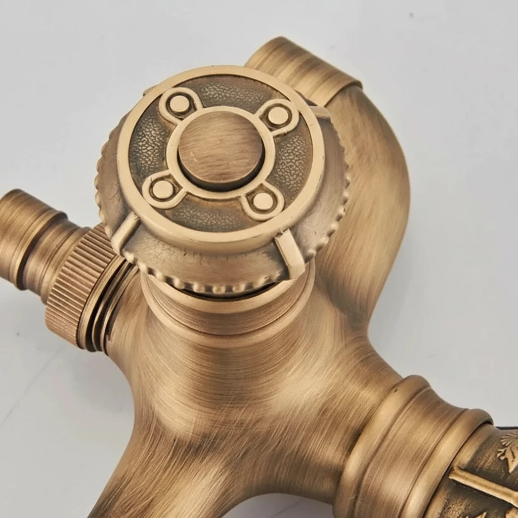 Close-up of the Allfixture Antique Brass Bidet Faucet Wall Mounted Carved Bidet Faucet, showcasing an intricate, circular handle. The wall-mounted faucet features detailed engravings and a rustic finish that impart an antique appearance. The valve has three connection points and textured ridges for grip and control, pairing beautifully with an ornate shower head.