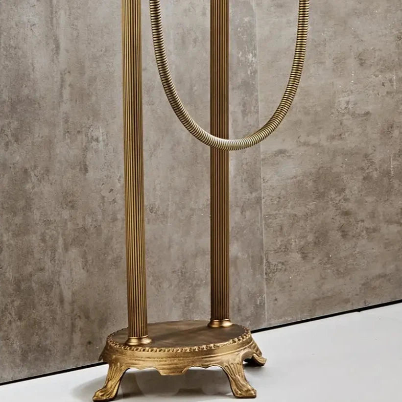 A close-up of the Allfixture Antique Brass Floor Standing Bathtub Faucet Tub Filler with an ornate clawfoot-style base and flexible metal hose, set against a beige tiled wall and white floor.