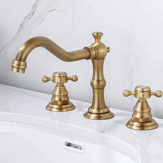 The Allfixture Maison Brass Widespread Bathroom Faucet features a curved spout and two cross-handle knobs, installed on a white countertop beside a sink and set against a marble-patterned wall.