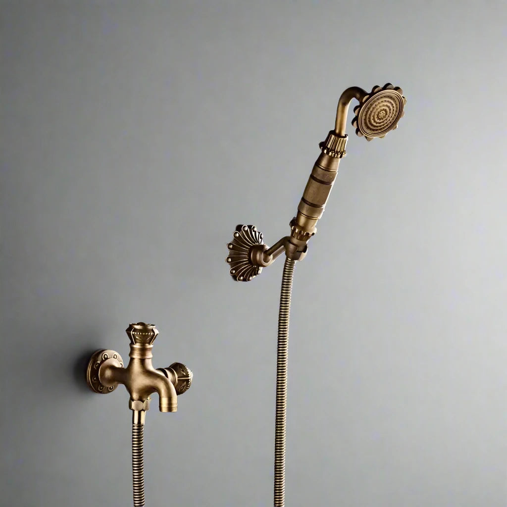 An Antique Brass Bidet Faucet by Allfixture, featuring an ornate handle and attached hose, is wall-mounted on a tiled surface. Below the bidet faucet is a matching valve with a decorative mount and intricate faucet, all in the same elegant brass finish.