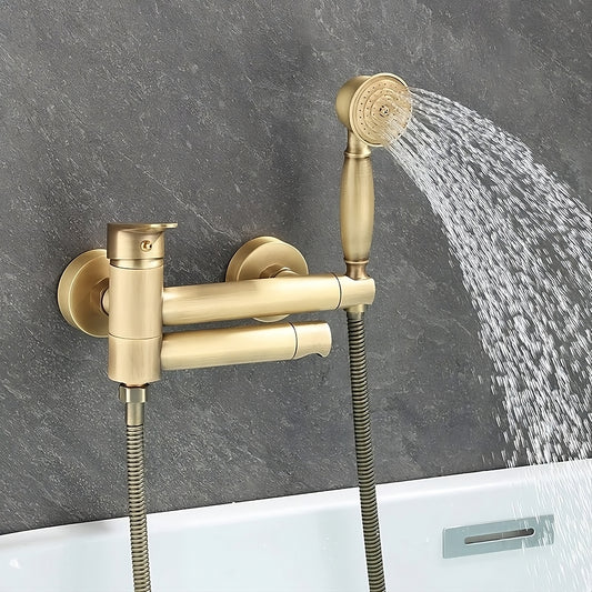 The Tiqui Maison Bathtub Faucet With Shower Head in gold antique brass is wall-mounted, featuring a handheld showerhead that sprays over a bathtub, beautifully complemented by a gray textured wall.