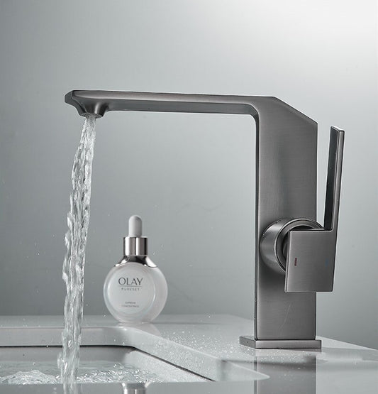 A modern, angular Tiqui Valmont Single Handle Bathroom Sink Faucet pours water into a white sink, while an Olay serum bottle with a dropper rests on the countertop in the background.