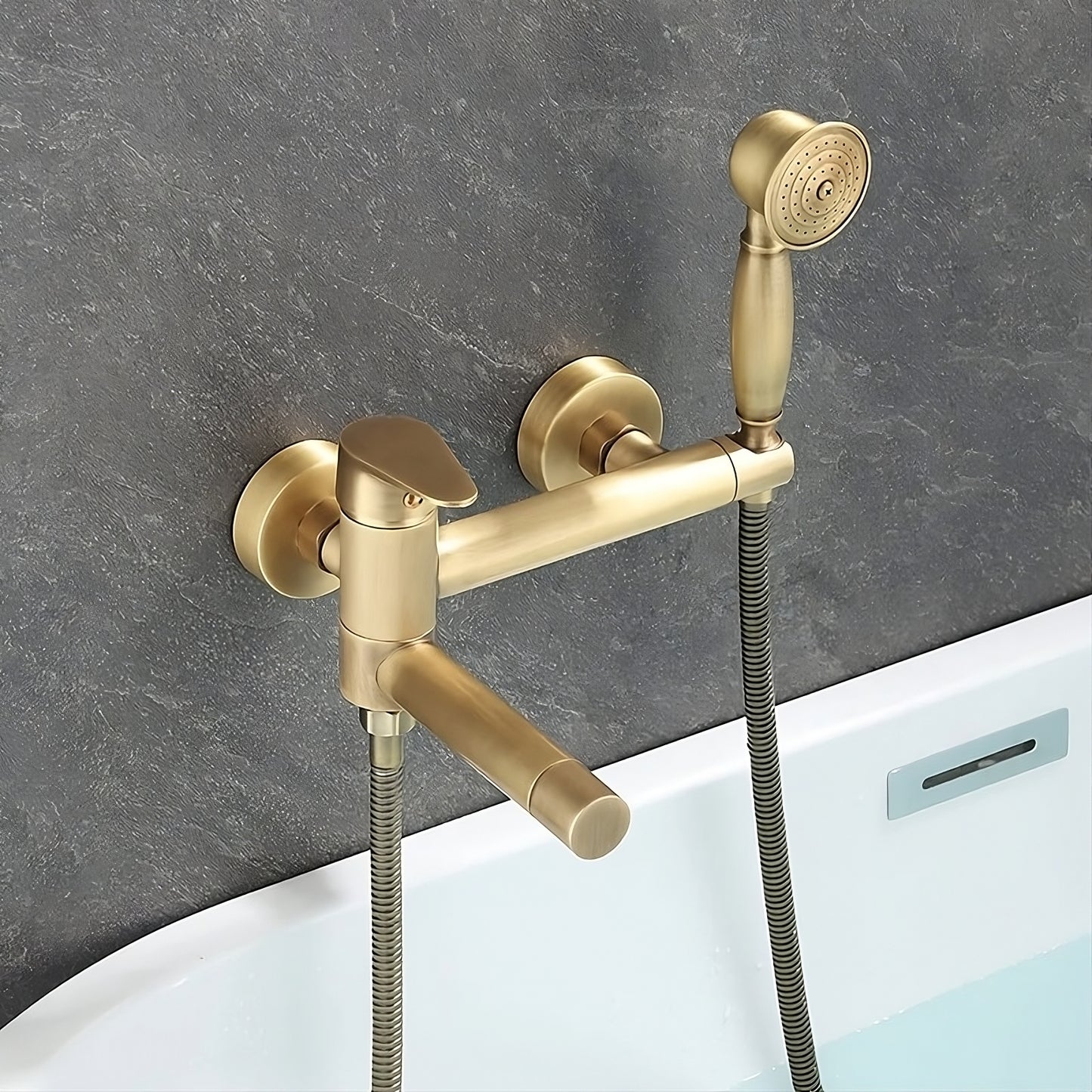 The Tiqui Antique Brass Handheld Shower Head With Bathtub Faucet is a modern, wall-mounted set installed against a textured, dark gray wall above a white bathtub. It features a handheld showerhead with water streaming out and a sleek bathtub faucet.