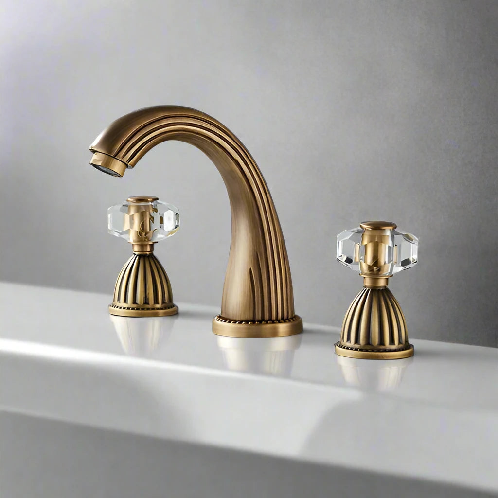 The Allfixture Heritage Widespread Basin Faucet features a gold-toned finish and crystal-style handles on a white sink with a gray backdrop. Its 3-hole configuration adds elegant, vintage-inspired charm.