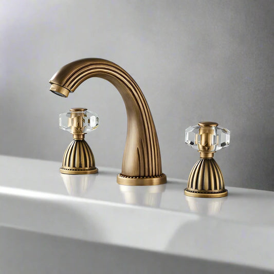 The Allfixture Heritage Widespread Basin Faucet features a gold-toned finish and crystal-style handles on a white sink with a gray backdrop. Its 3-hole configuration adds elegant, vintage-inspired charm.