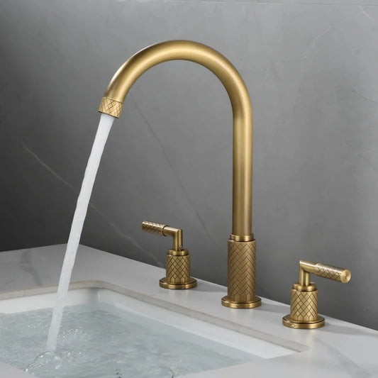 The Mike Jake Windsor Widespread Bathroom Faucet, finished in gold-colored antique brass, features a high curved spout and two matching handles on each side, elegantly installed with a white sink against gray marble and a white countertop.