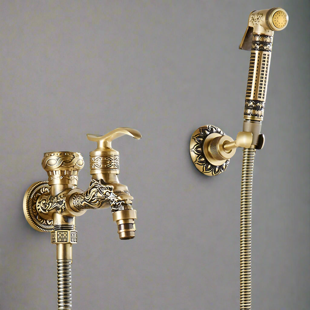 The Tiqui Wall Mounted Antique Brass Toilet Sprayer Bidet Faucet features a handheld sprayer with intricate patterns, antique bronze finish, flexible hoses, and is mounted on a gray wall.