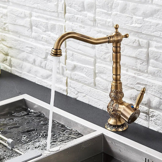 The Rozin Heritage Single Handle Kitchen Faucet in antique brass adds vintage charm and ornate detailing as it streams water into a modern stainless steel sink, set against a textured white brick backsplash.