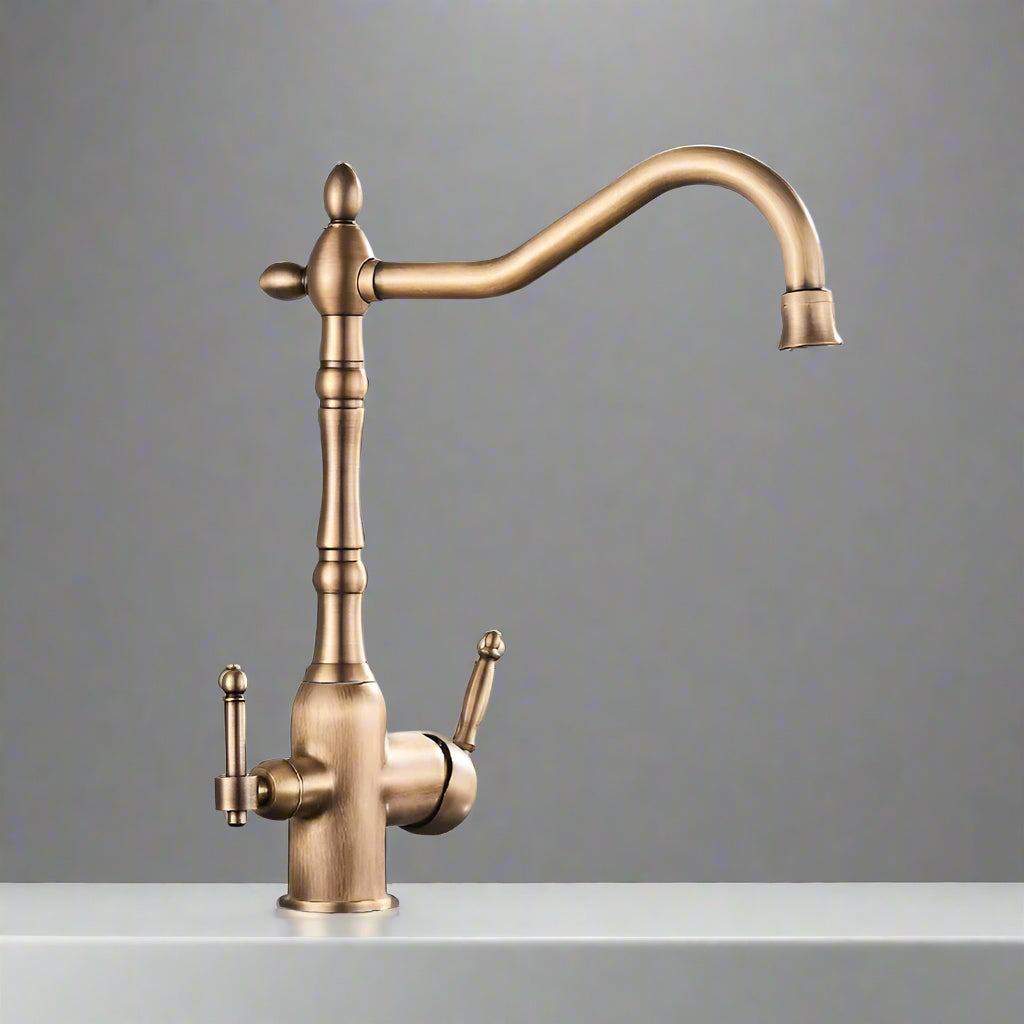 A sleek Uythner Dual Handle Solid Brass Faucet With Filtered Water Tap, featuring a vintage design, is mounted on a gray countertop. Water flows from the curved spout into a stainless steel sink below. In the background, a white bowl with a decorative pattern rests beside vegetables. Light filters through blinds, highlighting the elegant fixture.