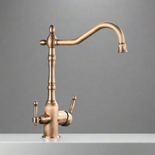 A sleek Uythner Dual Handle Solid Brass Faucet With Filtered Water Tap, featuring a vintage design, is mounted on a gray countertop. Water flows from the curved spout into a stainless steel sink below. In the background, a white bowl with a decorative pattern rests beside vegetables. Light filters through blinds, highlighting the elegant fixture.