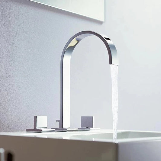 A sleek, modern Double Handle Deck Mounted Bathroom Sink Faucet from AllFixture with a high arch design is flowing water into a dark sink. The chrome fixture, reminiscent of a stylish shower head with its reflective finish, is set against a textured gray wall. The clear sink water ripples gracefully under the constant stream from the faucet.