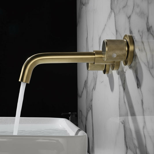 The Tiqui Windsor Wall Mounted Bathroom Faucet features textured dual handles and a solid brass build, pouring water into a white rectangular sink set against a dark matte wall.