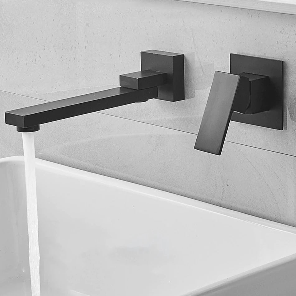 An AllFixture Wall Mount Swivel Spout Wash Basin Bathroom Faucet, featuring a modern, chrome-plated design with minimalist elements, pours a steady stream of water against a light gray tiled wall. The faucet has a sleek, rectangular form that enhances the contemporary aesthetic of the bathroom setting.