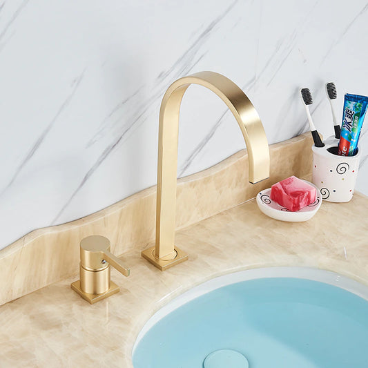 A marble countertop with a light blue sink features the allfixture Valmont Solid Brass Bathroom Sink Faucet, a matching soap dispenser, a cup with two toothbrushes, toothpaste tube, and a dish holding pink soap.