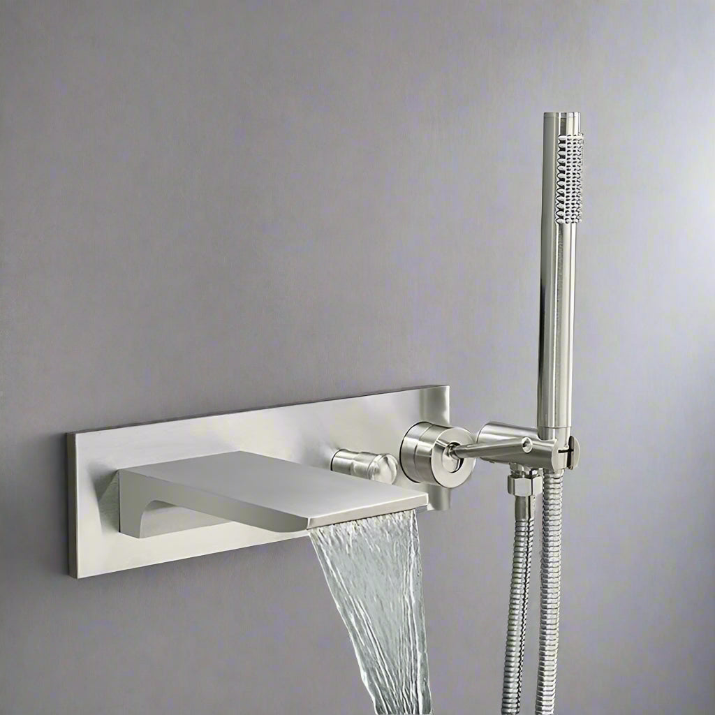 The Sekova Wall-Mounted Brass Bathtub Faucet features a flat spout, an attached handheld shower sprayer, and a sleek metal plate design, making it perfect for modern bathrooms with a minimalist gray wall backdrop.