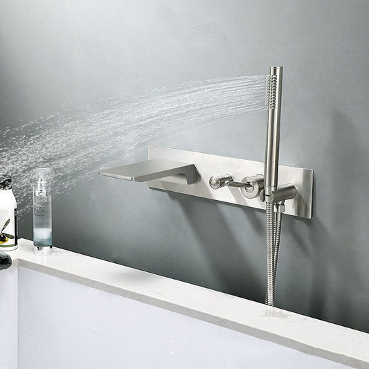 The Sekova Wall-Mounted Brass Bathtub Faucet with Handheld Shower Sprayer is shown spraying water against a gray wall beside a white tub, with toiletries visible on the bathtub’s edge.