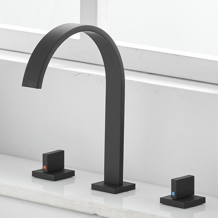 A minimalist black sink faucet from AllFixture, featuring an arching design, is mounted on a white countertop. The Double Handle Deck Mounted Faucet includes two lever handles—one on each side—with subtle red and blue indicators for hot and cold water respectively. In the background, a white window sill completes the scene.