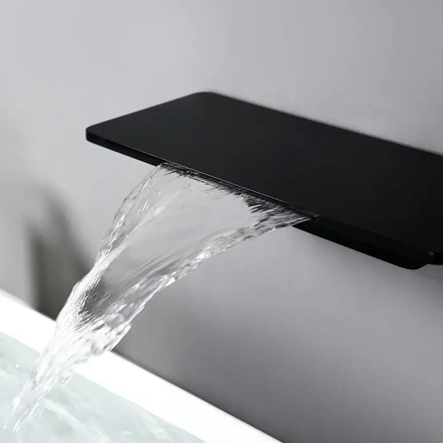 A minimalist bathroom sink features a rectangular white basin. Water flows gracefully from the Bagnox™ Wall Mounted Waterfall Brass Faucet by AllFixture, which doubles as a shelf holding two small bottles. The elegant setup is mounted on a light gray wall, near matching bathroom faucets, and part of a plant is visible on the left.