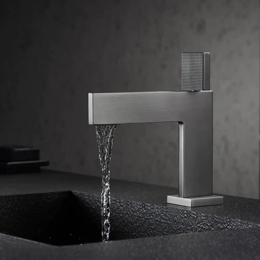 The Mike Jake Valmont Single Handle Bathroom Sink Faucet, with a modern matte finish, pours water into a black textured sink set against a gray minimalist background.