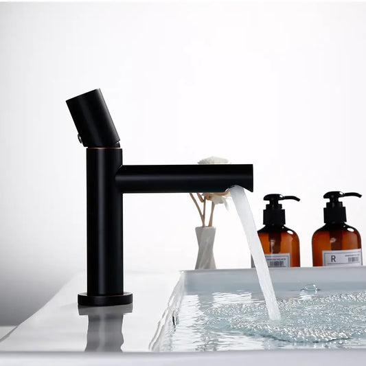 A modern Bagnolux Wasser™ Solid Brass Single Handle Bathroom Sink Faucet in black and copper with a cylindrical design is mounted on a white sink. The water flows smoothly from the faucet into the sink, while the handle is positioned at an angle on the side for easy access.