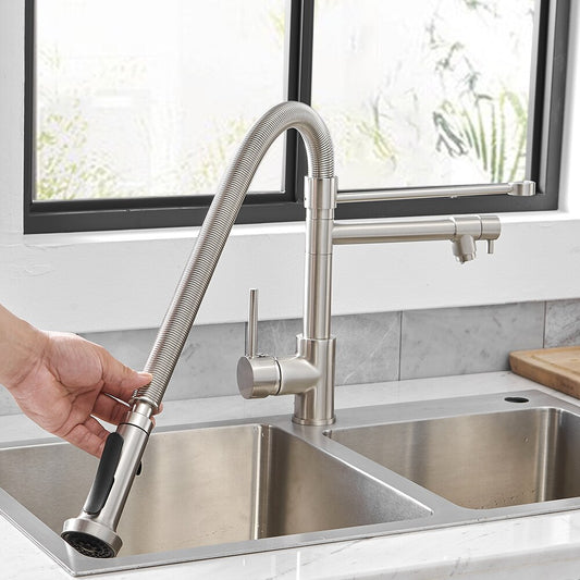 A hand pulls down the flexible sprayer of the AllFixture Ross Double Spout LED Kitchen Faucet, which is mounted over a double sink with a bright window and tiled backsplash in the background.