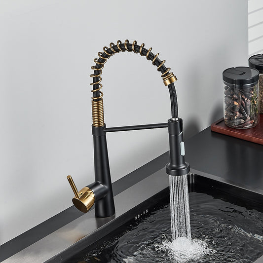 A modern Rozin Deck Mounted Pull Down Sprayer Kitchen Sink Faucet, featuring a sleek black finish with gold accents, is installed over a stainless steel sink. The faucet boasts a curved, flexible spring spout with a convenient pull-down sprayer. In the background, jars and a white panel on the wall enhance the sleek design.