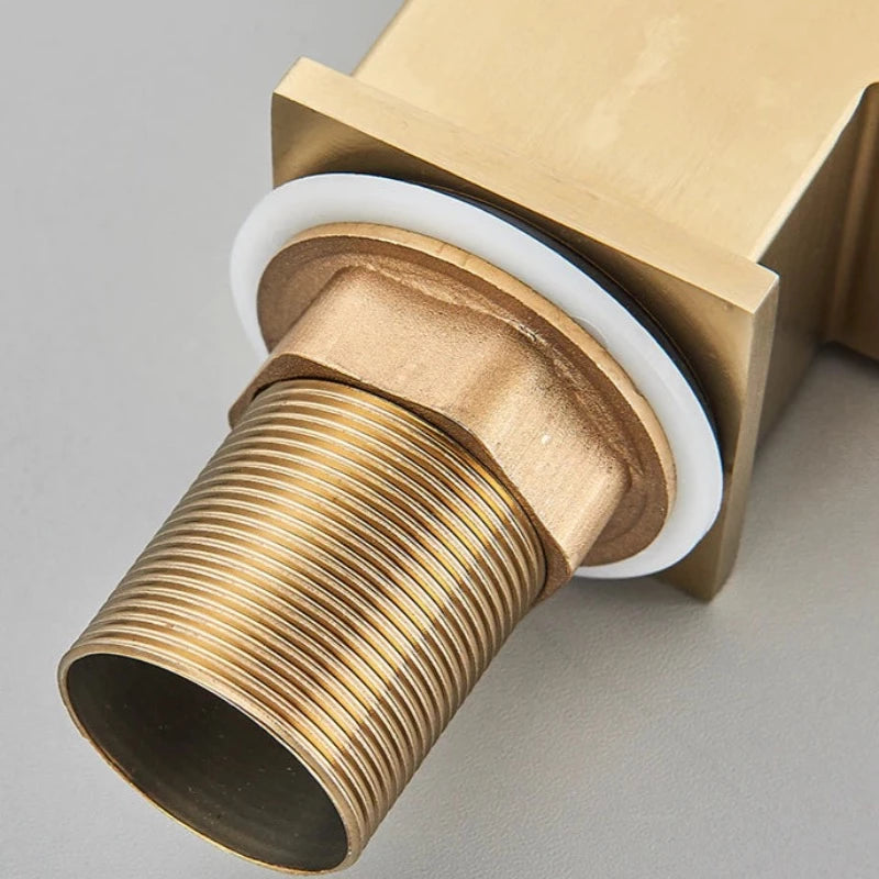 The Deck Mounted Single Handle Kitchen Faucet by Rozin, with its sleek and minimalist brushed gold finish, releases a steady stream of water into a stainless steel sink. It features a right-angled spout and an angular handle, set against a plain, light-colored wall.