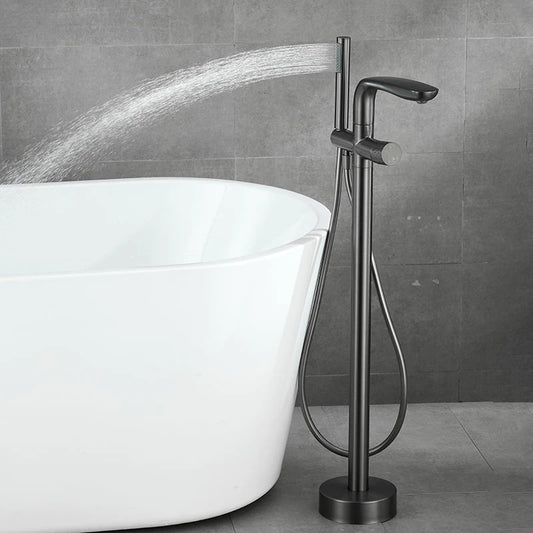 A Mike Jake Floor Mounted Bathtub Faucet Shower Mixer with a minimalist design is positioned next to a sleek, white bathtub. Water flows from the faucet into the bathtub, set against a backdrop of gray tiled walls and flooring that enhance the contemporary aesthetic, complete with stylish bathroom faucets throughout.