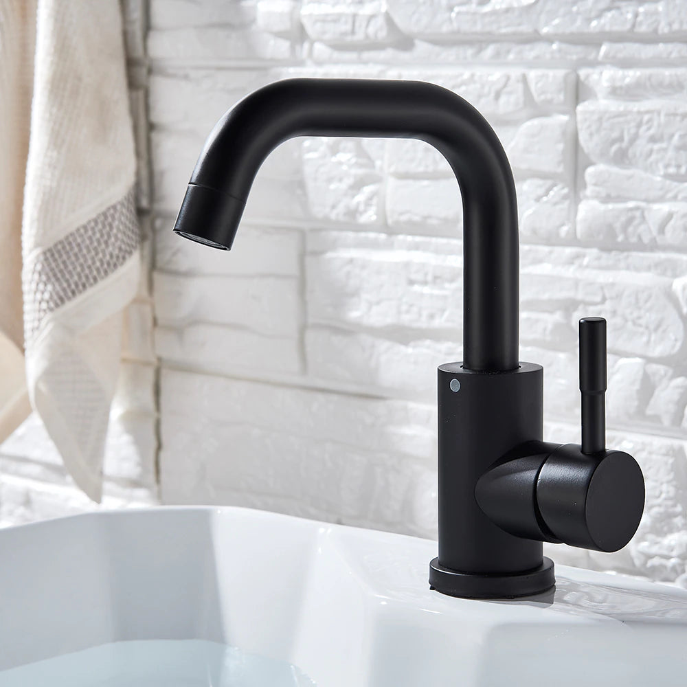 The Wasser™ Deck Mounted Single Handle Bathroom Sink Faucet by MyQualife, featuring a sleek, curved design in modern black, is installed on a white sink. Behind the sink is a white, textured brick wall, with a white towel adorned with a beige stripe hanging nearby.