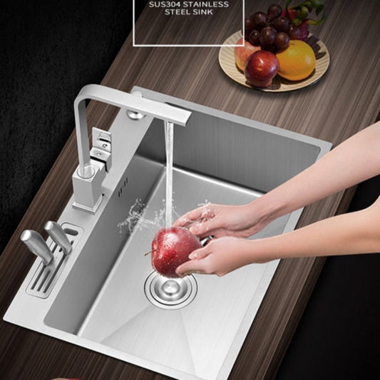 An AllFixture Stainless Steel Topmount Kitchen Sink With Knife Holder, featuring a built-in cutting board, a sleek kitchen faucet, and a sliding drain tray. The sink is set against a backdrop of a nighttime city skyline seen through a window, with apples and tomatoes on the nearby cutting board.