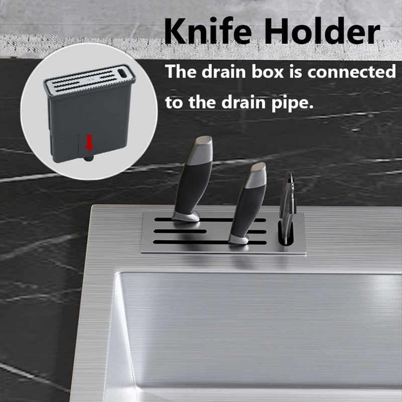 An AllFixture Stainless Steel Topmount Kitchen Sink With Knife Holder, featuring a built-in cutting board, a sleek kitchen faucet, and a sliding drain tray. The sink is set against a backdrop of a nighttime city skyline seen through a window, with apples and tomatoes on the nearby cutting board.