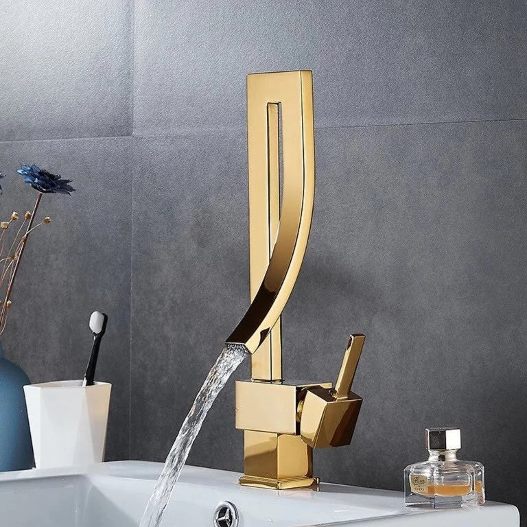 A modern, sleek Deck Mounted Brass Bathroom Basin Faucet from Bacala, featuring a curved design in black, is dispensing water into a white sink. In the background, there's a vase with dried flowers and a toothbrush holder containing a black and white toothbrush. The wall appears to be tiled in a dark color, echoing the elegance of a premium shower head.