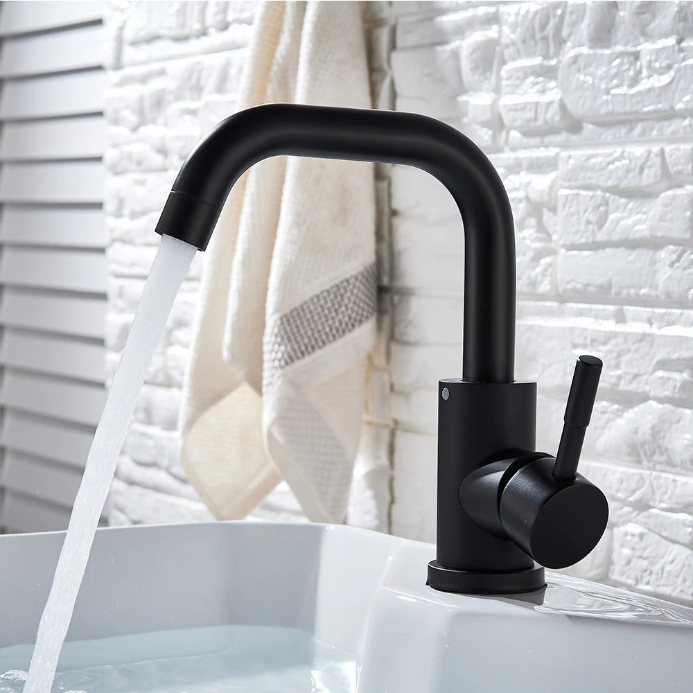 The Wasser™ Deck Mounted Single Handle Bathroom Sink Faucet by MyQualife, featuring a sleek, curved design in modern black, is installed on a white sink. Behind the sink is a white, textured brick wall, with a white towel adorned with a beige stripe hanging nearby.