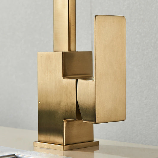 Close-up of the Valmont Single Handle Kitchen Faucet by Rozin, featuring a modern gold-toned finish with geometric lines on a light surface, set against a textured gray wall—evoking elegant, contemporary style.