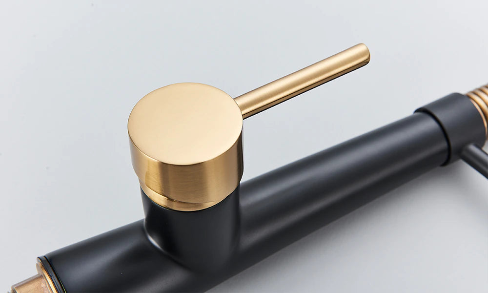 A modern Rozin Deck Mounted Pull Down Sprayer Kitchen Sink Faucet, featuring a sleek black finish with gold accents, is installed over a stainless steel sink. The faucet boasts a curved, flexible spring spout with a convenient pull-down sprayer. In the background, jars and a white panel on the wall enhance the sleek design.