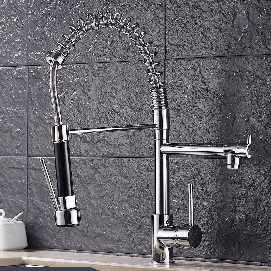 An allfixture Solid Brass Pull Out Spring Spout Kitchen Faucet with a flexible, coiled stainless steel spring neck and a black handle is installed against a dark tiled backsplash. The faucet features two spouts and a lever handle for temperature and flow control. A white jar sits on the counter in the background.