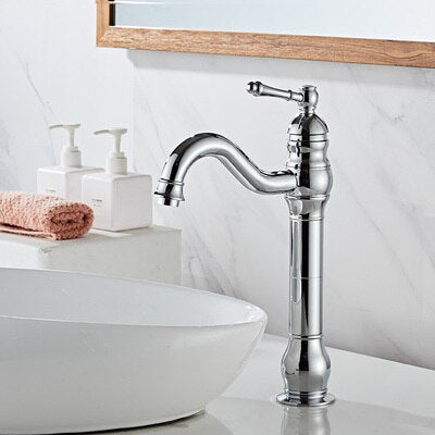 A Tiqui Deck Mounted Single Handle Bathroom Faucet is dispensing water into a decorative ceramic sink. A textured cloth is partially submerged in the water, draped over the edge of the sink. The background features a dark, textured wall surface.