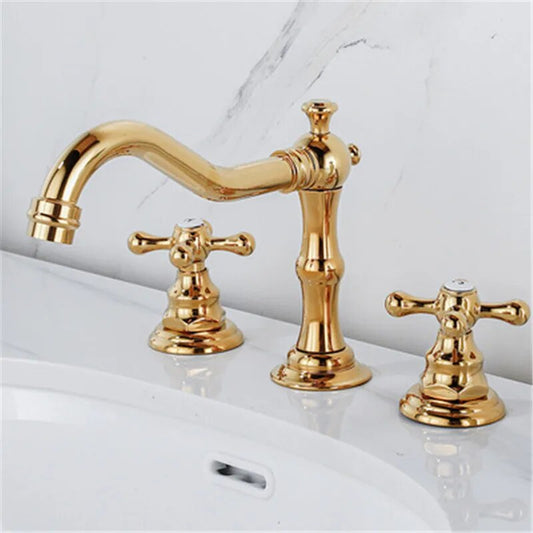 A polished gold Dual Handle Solid Brass Deck Mounted Bathroom Faucet from Tiqui set on a white countertop. The set features a curved spout with elegant detailing and two cross-handle knobs for hot and cold water control. The background is white with gray veining, resembling marble—truly an exquisite choice among bathroom faucets.