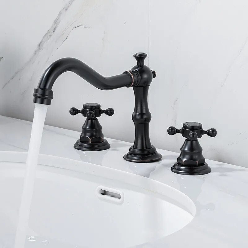 A polished gold Dual Handle Solid Brass Deck Mounted Bathroom Faucet from Tiqui set on a white countertop. The set features a curved spout with elegant detailing and two cross-handle knobs for hot and cold water control. The background is white with gray veining, resembling marble—truly an exquisite choice among bathroom faucets.